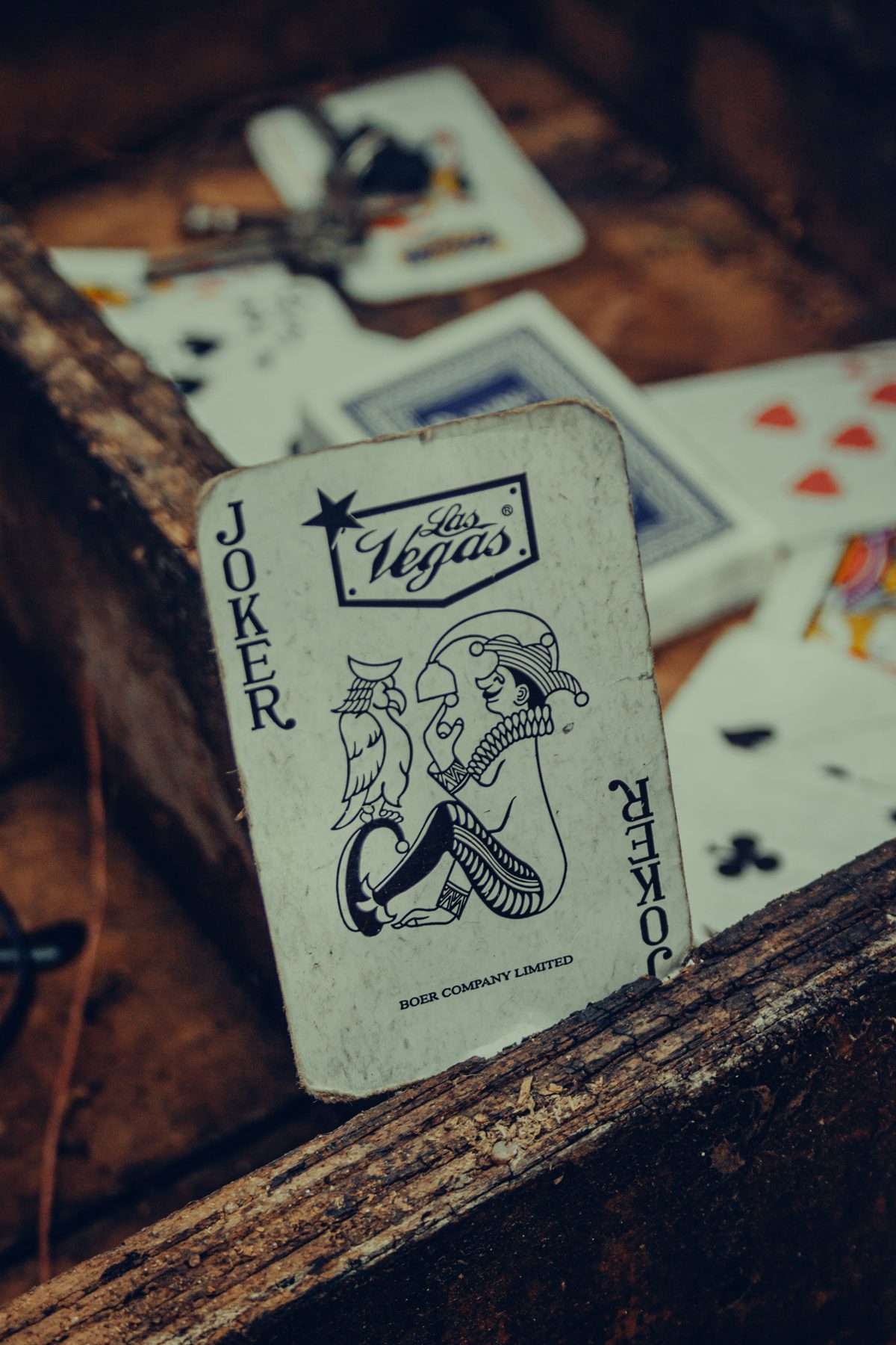 A worn Joker playing card propped against a wooden beam